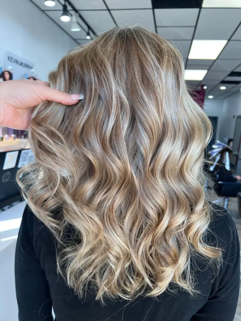 Dimensional blonde balayage styled in defined curls, seen from behind
