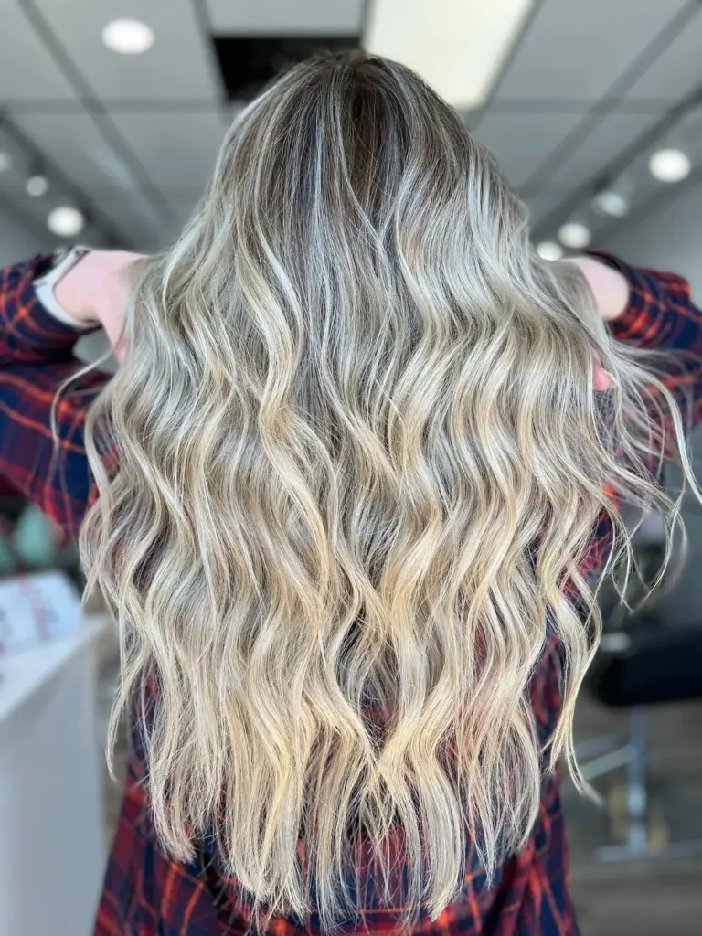 Bright blonde balayage with a soft shadow root, styled in long waves