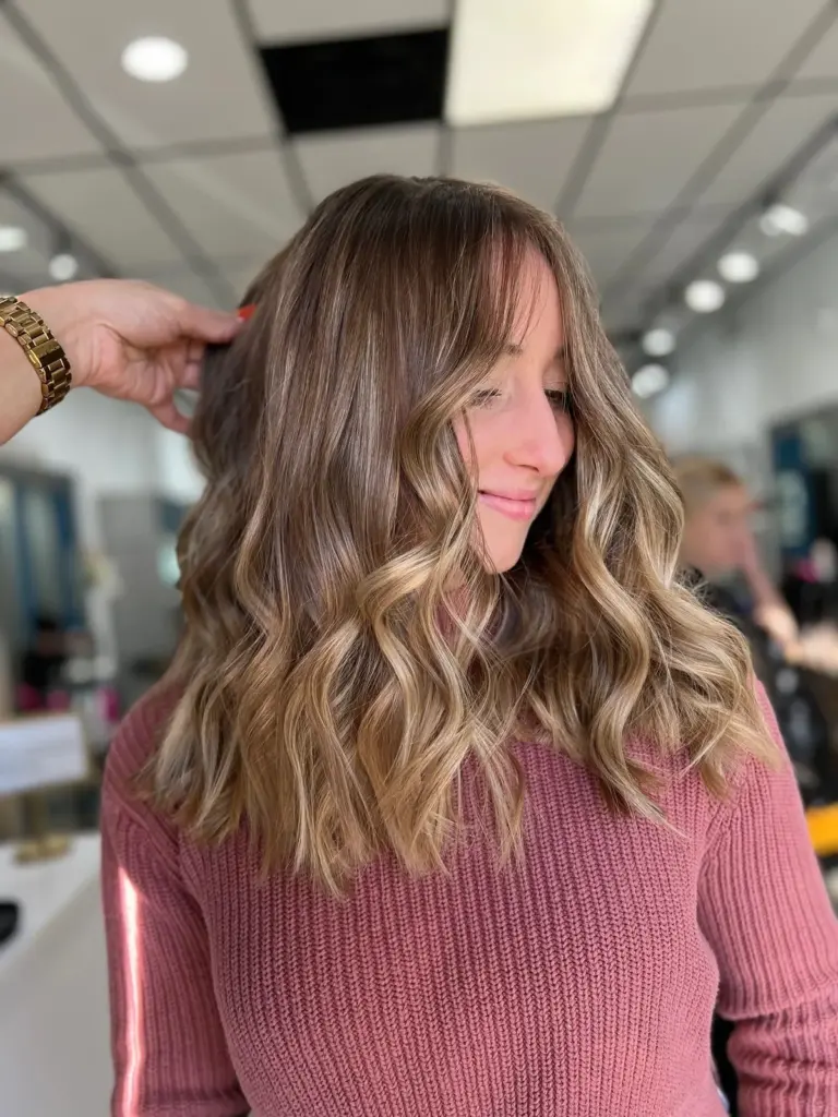 Caramel-blonde balayage with curtain bangs and loose waves