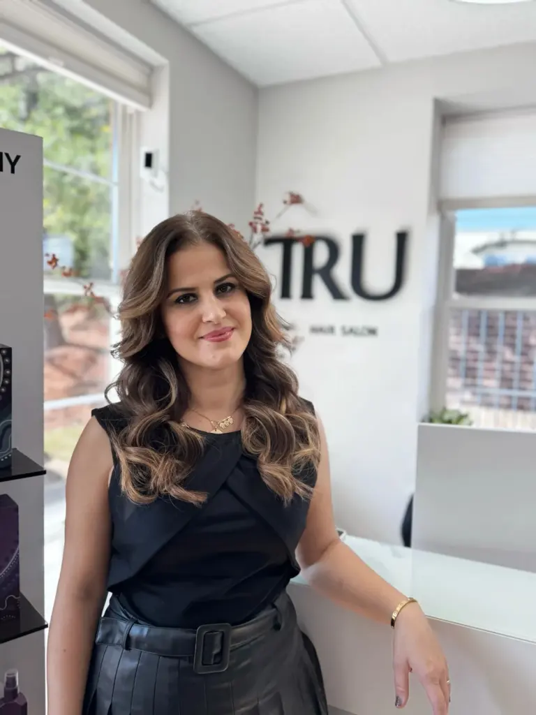 Eri, cosmetologist at TRU Salon, beside the salon's TRU sign