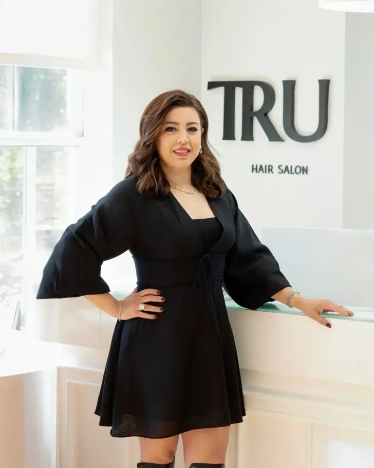 Sama, founder and master stylist of TRU Salon, in front of the salon's TRU Hair Salon sign